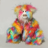 Cock A Doodle Doo, a colourful, furry teddy bear with a shaggy, multi-hued coat in pink, yellow, blue, orange, and green, sitting against a plain light grey background.