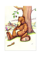 A birthday card showing a bear asleep under a tree with a brightly coloured bird shouting "Wake up it's your birthday"