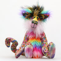 Faustus is mostly made from a very bright and colourful, monstrous cotton fabric. The sides of Faustus' face are a very long pale pink mohair with a dusky lavender-pink backcloth and the top of his nose is a long, fluffy mohair hand dyed yellow. His tummy and the backs of his ears are a long faux fur in bands like a rainbow and on top of his head he has a long black faux fur with plumes of yellow, magenta and teal. Faustus' footpads are made from hand dyed velvet.