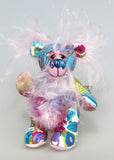 Tim Tickletum is made from a beautiful, cotton fabric printed with a batik design in blue, turquoise, rose and pink. His face and the backs of his ears are a long wispy dusky pink mohair and his tummy and the underside of his tail are a shorter, denser mohair in blue, purple and violet. Tim has hand dyed, velvet paw pads. Tim Tickletum has beautiful hand painted eyes with hand coloured eyelids, an intricately embroidered nose sewn from individual threads and a broad, sweet smile