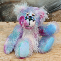 Tim Pimpling is a happy, little one of a kind, mohair artist bear by Barbara-Ann Bears. Tim stands 6.5 inches( 16 cm) tall and is 5 inches ( 13 cm) sitting. He is mostly made from a medium length, slightly distressed and fluffy mohair that Barbara has hand dyed in sky blue with some splashes of magenta, pink and lilac